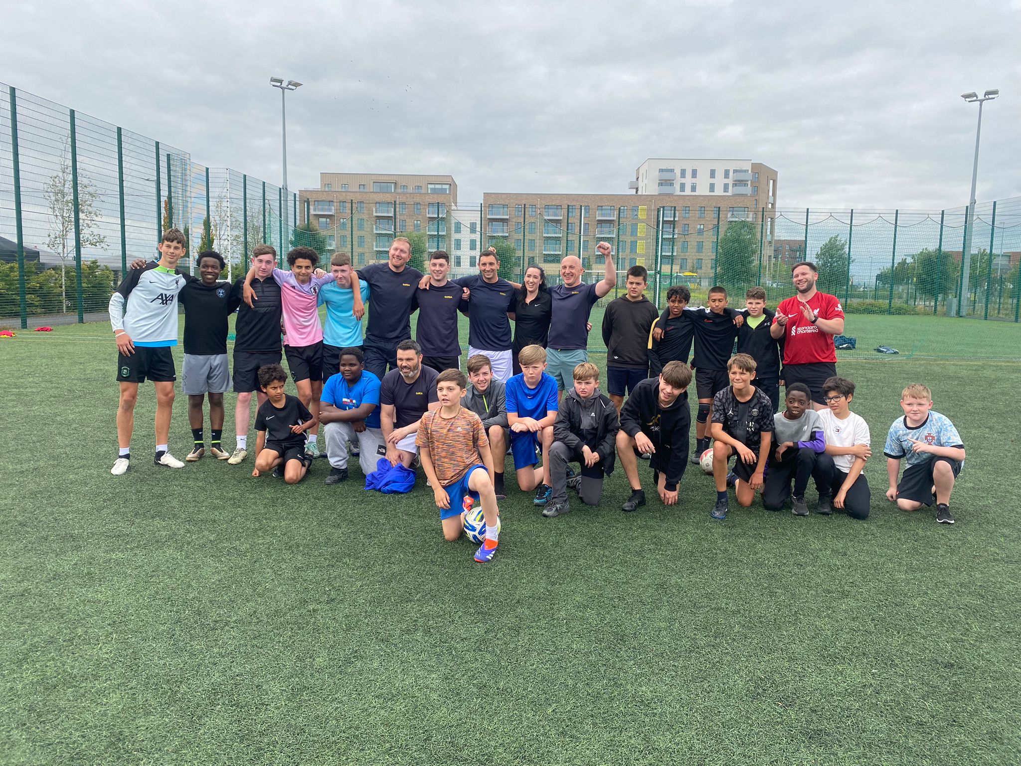 Group of young people and coaches posing together on a football pitch after training Group of young people and coaches posing together on a football pitch after training