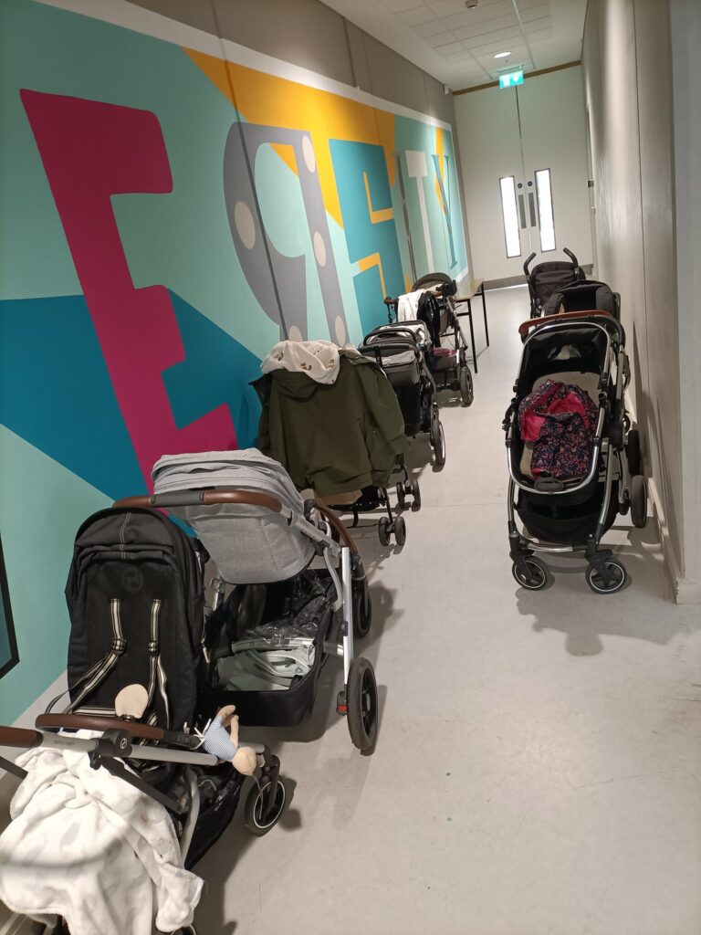 Several baby prams lined up along a colorful corridor wall