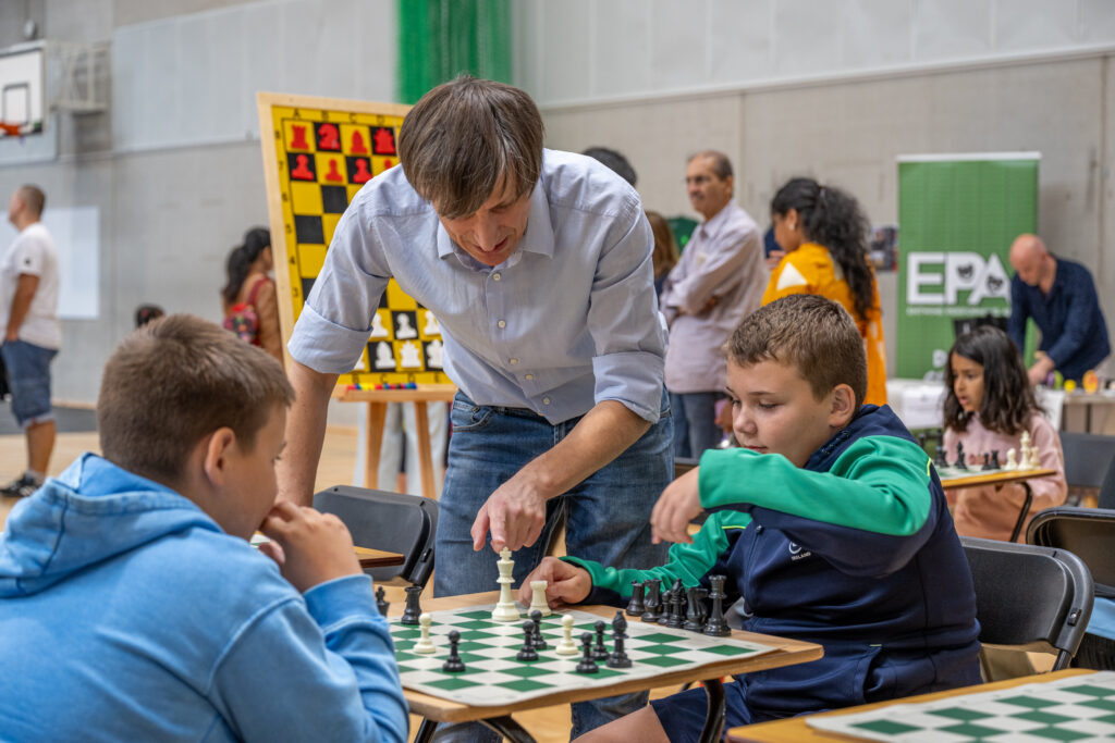 Children playing chess while an instructor gives guidance at a community event